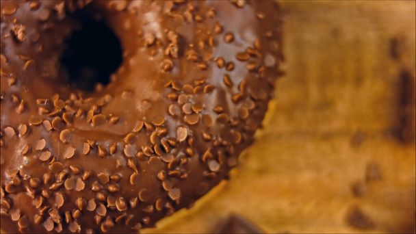 Schokoladen-Donuts mit Schokoladenstücken verziert. Donuts stehen auf einem Papier, das mit natürlicher Schokolade verziert ist. Makro- und Schiebereglerschießen. Bäckerei- und Lebensmittelkonzept. Verschiedene bunte Donuts. Schokolade, rosa - Foto, Bild