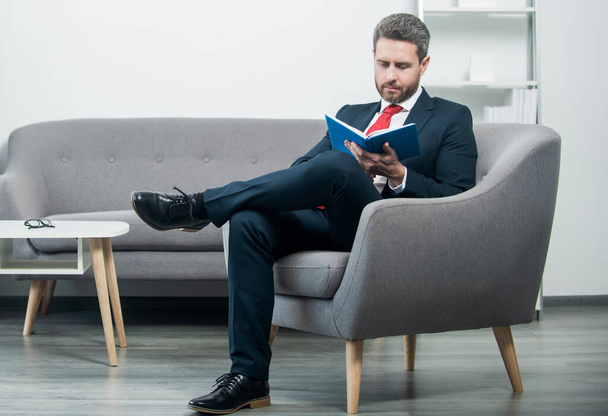 maturo uomo d'affari in abito sedersi in ufficio leggere libro. - Foto, immagini