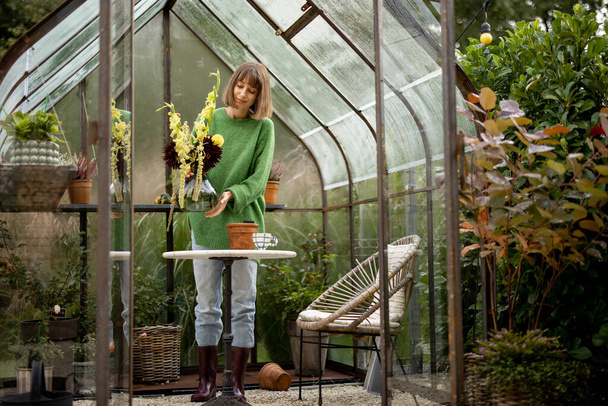 Junge Frau kümmert sich um Blumen, gießt schönen Blumenstrauß in winzigen Orangerie im Garten. Hobby des Pflanzen- und Blumenanbaus - Foto, Bild