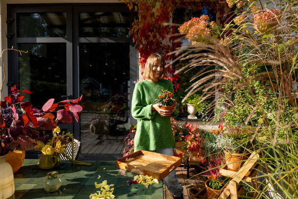 Frau kümmert sich im Herbst um Pflanzen und Blumen im Garten. Schöne Blätter in gelben und roten Farben - Foto, Bild