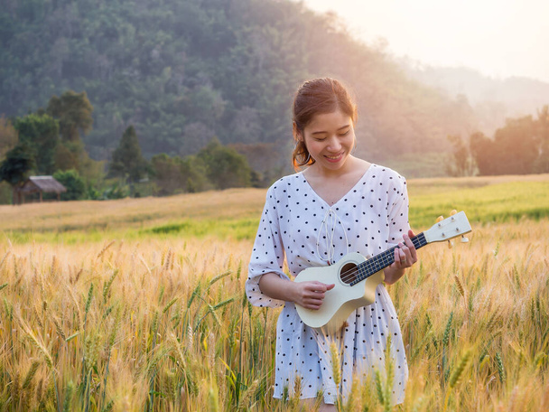 Asian woman with ukulele in barley field at sunset time - Fotoğraf, Görsel