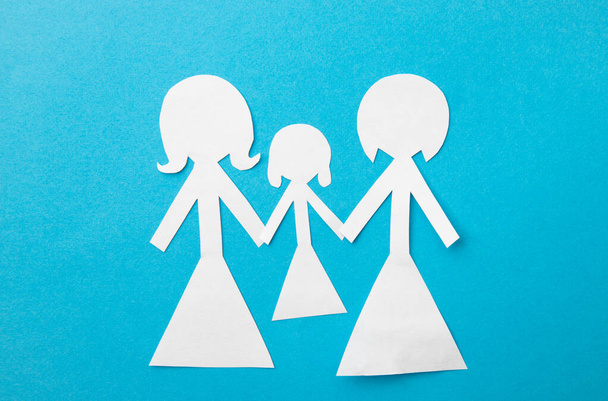 Έννοια υιοθεσίας ζευγαριού του ίδιου φύλου. Κούκλες χαρτί δύο μητέρες κρατώντας τα χέρια των απογόνων σε μπλε φόντο. - Φωτογραφία, εικόνα