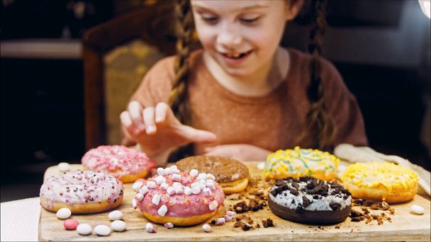 The girl chooses from several gifts, she points her finger. Chocolate, marshmello and candy donuts on a retro baking tray. Donuts are on a paper decorated with natural chocolate. Macro and slider - Photo, Image