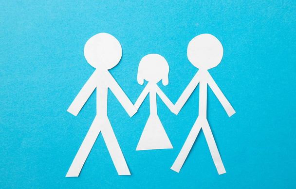 Идея усыновления однополых пар. Бумажные куклы два отца держась за руки потомства на синем фоне. - Фото, изображение