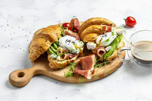 Croissant prosciutto, buggyantott tojás, jamon kék, sajt, avokádó, mikrogin és cseresznye paradicsom. Mediterrán előétel. Reggeli koncepció. - Fotó, kép
