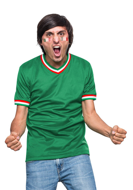 Soccer fan man with jersey and face painted with the flag of the Mexico team screaming with emotion on white background. - Foto, afbeelding