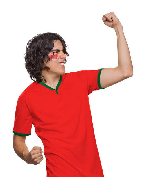 Soccer fan man with jersey and face painted with the flag of the Morocco team screaming with emotion on white background. - Foto, imagen