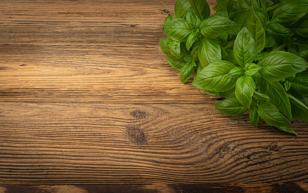 Fresh basil on wood table background. Green basilic bunch on rustic wooden desk plate, fresh basil mockup, copy space - Photo, Image