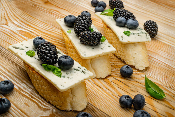 Blue cheese on bread. Gorgonzola with berries and honey, bruschetta with ricotta, blueberries and blackberries, french toasts on wooden rustic background - Fotó, kép