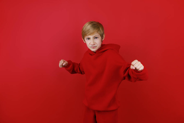 Ένα αγόρι με κόκκινη φόρμα έσφιξε τις γροθιές του και τις έβαλε μπροστά. - Φωτογραφία, εικόνα