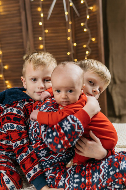 tres hermanos en pijama de navidad, fondo de navidad con estrellas doradas y guirnaldas brillantes. Foto de alta calidad - Foto, imagen