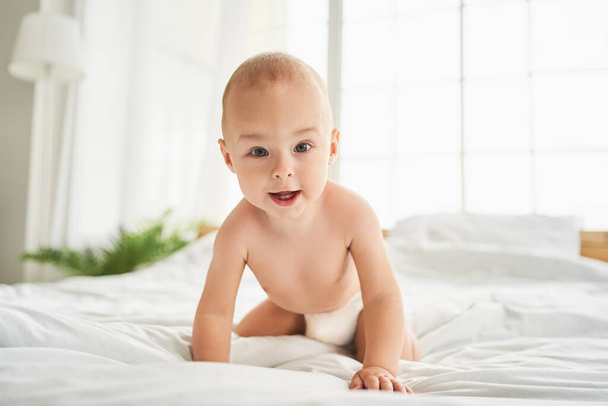 Close up portrait of a cute little small child caucasian infant toddler newborn smiling with baby milk teeth lying on the comfortable bed. Teething concept, childcare and parenthood. - Photo, image
