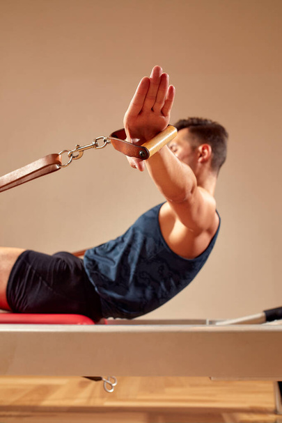Side view of barefoot male athlete lying on pilates reformer and performing abs exercise during fitness workout. Pilates man concept - Foto, imagen