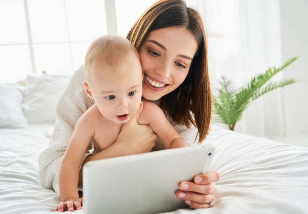 Caucasian white newborn baby is watching cartoons on a tablet. Little child using technology. The development of education at an early age. Video chat, video call. - Photo, image