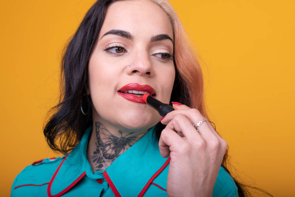 Beautiful caucasian woman applying a bright red color lipstick on her lips over yellow background - Photo, Image