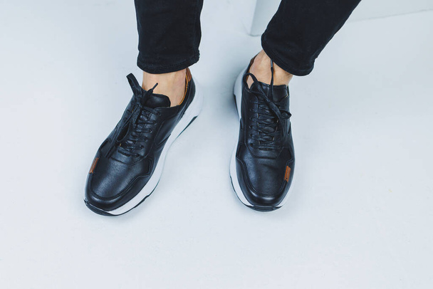 Men's legs in casual shoes of black color made of genuine leather, men on shoes in black sneakers. High quality photo - 写真・画像