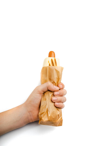 Hand holding hotdog. Sausage inside a grilled bun, minimal hot dog in hand, fast food from the nearest store, hotdog on a white background - Photo, Image