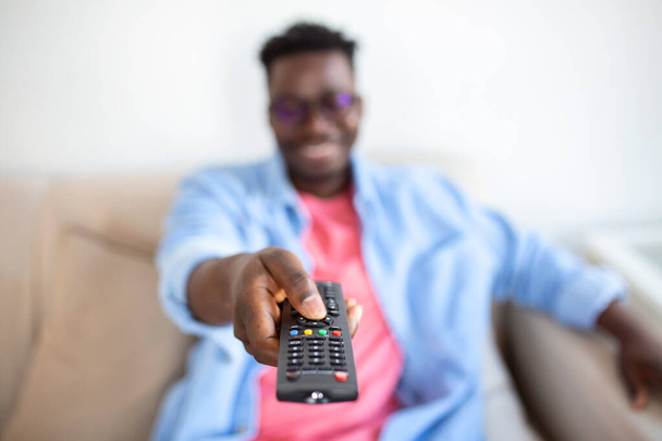 Innoissaan Afrikkalainen Amerikkalainen mies osoittaa televisio-ohjain kameran vaihto kanavat television katselu. Televisio-ohjelmamainos. Valikoiva fokus - Valokuva, kuva