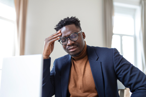 Stressed tired African American man touching temples, suffering from headache after long hours work, overworked overwhelmed businessman sitting at desk, feeling unwell - Photo, Image