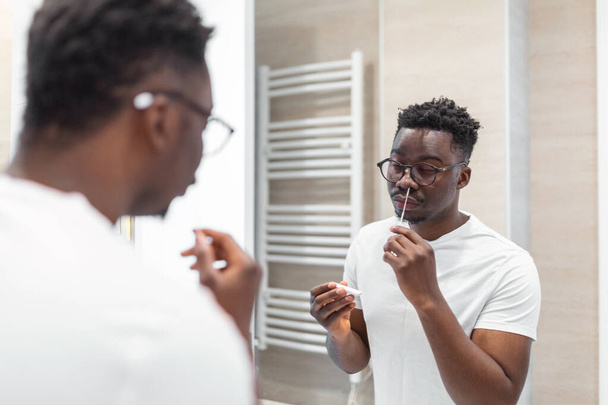 Afrikaanse man doet zelftest voor COVID-19 thuis met Antigen test kit. Coronavirus neusdoektest op infectie. - Foto, afbeelding