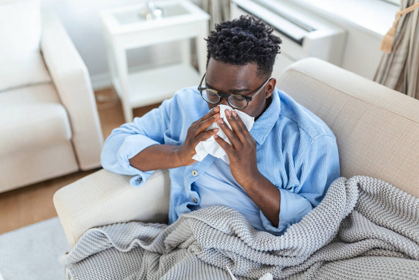 Kranke afrikanische junge Frau, die mit einer Decke bedeckt ist, bekommt Fieber, wenn sie erkältet niest, sitzt auf dem Sofa, krankes allergisches schwarzes Mädchen mit Allergiesymptomen, die zu Hause husten, GrippekonzeptKranker afrikanischer junger Mann, der mit einer Decke bedeckt ist - Foto, Bild