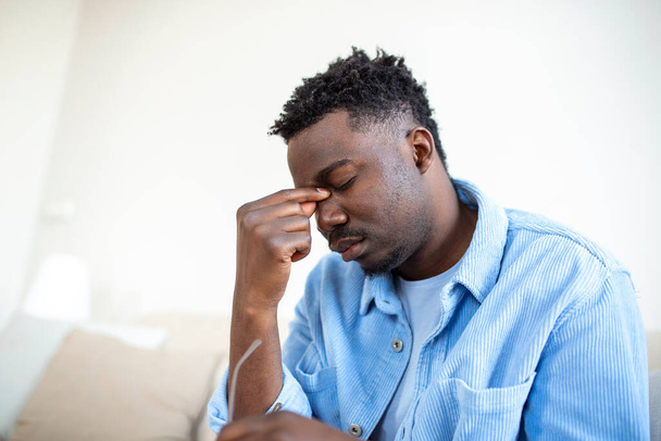 Unavený Afroameričan sundávající brýle, vyčerpaný masážní nosní most, po dlouhé práci s počítačem trpící oční námahou, pocit bolesti, koncepce zdravotního problému - Fotografie, Obrázek
