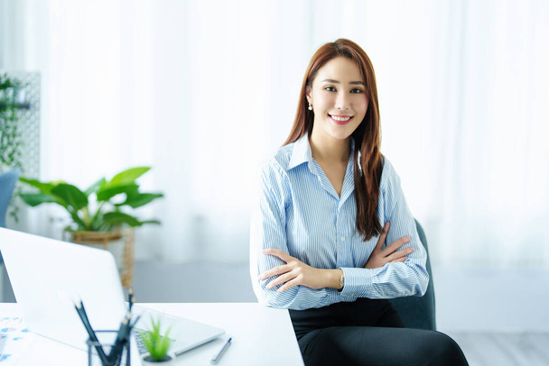 An Asian entrepreneur or businesswoman shows a smiling face while working with using computer on a wooden table - Photo, Image