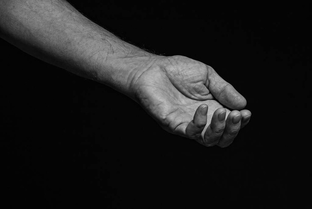 Το τεντωμένο ζαρωμένο αριστερό χέρι ενός ηλικιωμένου ζητά βοήθεια σε μαύρο φόντο. Μαύρο και άσπρο. - Φωτογραφία, εικόνα