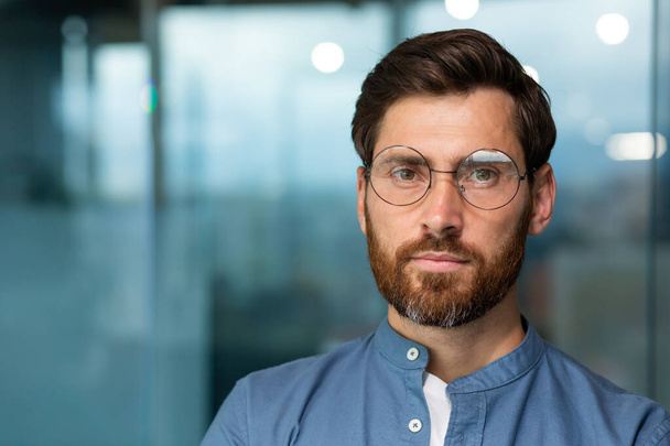 Close-up portrait of serious and thoughtful mature businessman with beard, man in shirt and glasses looking at camera, startuper working inside modern office building. - Foto, immagini