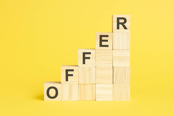 la palabra oferta está escrita en una pirámide de cubos de madera. bloques sobre un fondo amarillo brillante - Foto, Imagen