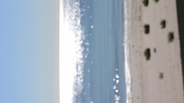 Fondo borroso abstracto.Manchas de reflejos blancos de sol brillante en la superficie azul de las olas del mar, cielo azul y playa de arena. Mar en día soleado. Textura bokeh natural. Lazo sin fisuras. Vídeo vertical - Imágenes, Vídeo