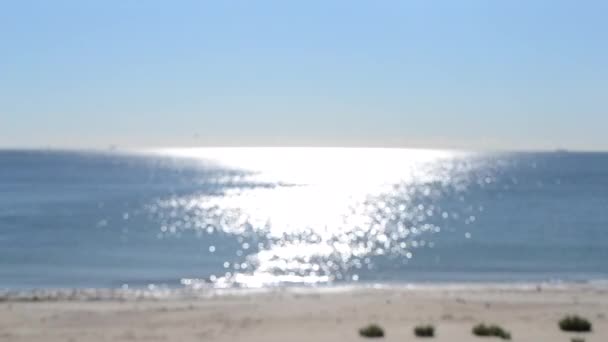 Fondo borroso abstracto.Manchas de reflejos blancos de sol brillante en la superficie azul de las olas del mar, cielo azul y playa de arena. Mar en día soleado. Fondo de textura bokeh borrosa natural. Lazo sin costura. - Imágenes, Vídeo