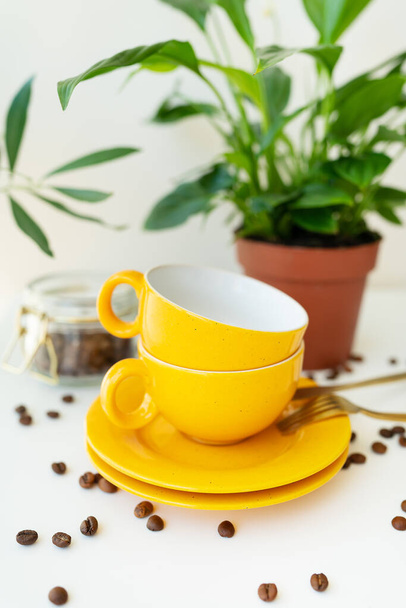 Piękny poranek, proces robienia kawy. Automatyczny ekspres do kawy kapanie stoi z żółtym kubkiem na białym stole, rozrzucone ziarna kawy. Zielony doniczka na tle - Zdjęcie, obraz