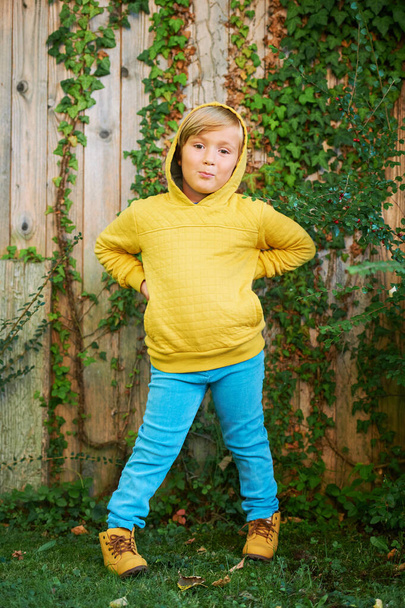 Portrait extérieur d'un adorable garçon de 5 ans portant un sweat à capuche jaune et un jean turquoise - Photo, image