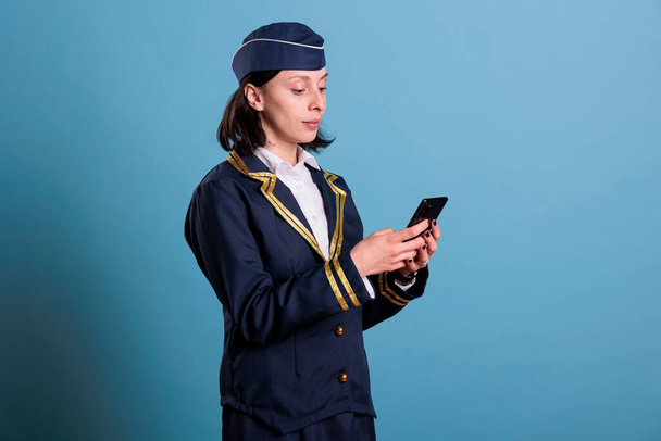 Flight attendant typing online message on smartphone, chatting on social media. Air hostess in uniform texting on mobile phone, browsing internet, messaging on telephone side view - Foto, imagen