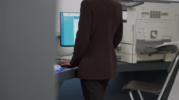 Réceptionniste afro-américain travaillant sur ordinateur avec rendez-vous et rapports médicaux papiers au comptoir d'enregistrement de l'hôpital. Travailleur clinique regardant les visites de contrôle sur moniteur à la réception. - Séquence, vidéo