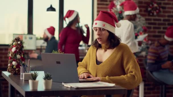 Diversas personas analizando la información sobre el ordenador portátil durante la festividad navideña en la oficina con árbol de Navidad. Trabajando en la computadora en el escritorio lleno de decoraciones de temporada y adornos. - Imágenes, Vídeo