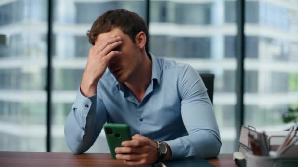 Tired businessman watching mobile phone screen at office. Perplexed boss thinking worrying work problems. Stressed professional surfing internet online at table. Unfocused ceo rubbing eyes alone  - Footage, Video