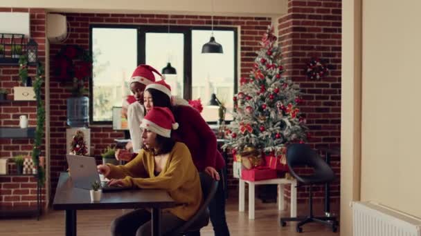 Multiethnic team of women doing teamwork in festive space, wearing santa hats and working on report. Brainstorming new startup ideas together during christmas holiday season with decorations. - Footage, Video