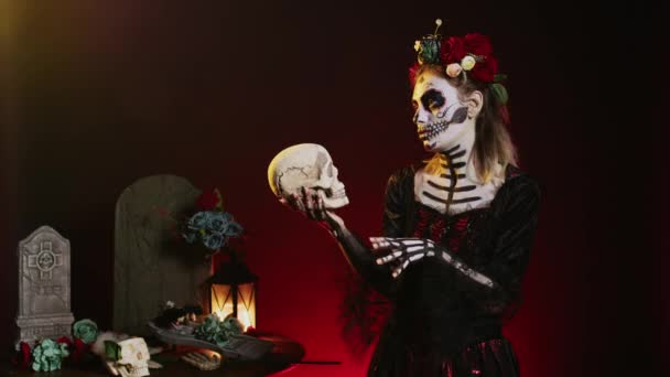 Strašidelná mrtvá žena držící svatou lebku ve studiu, chovala se děsivě a hrůzu, aby oslavila mexický halloween den. Flirtující bohyně v slavnostním kostýmu s tělesným uměním, vypadá jako dáma smrti. - Záběry, video