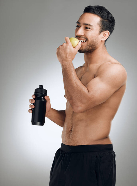 You do yourself a favour when you stick to a healthy diet. a man standing against a grey background while holding a bottle of water and an apple - Foto, Imagem