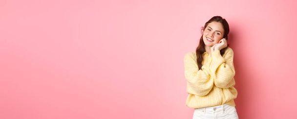 Schöne romantische Frau mit hellem Make-up und frühlingshaftem Outfit, schaut glücklich und erfreut in die Kamera, hält die Hände vor dem Gesicht, steht über rosa Hintergrund. - Foto, Bild