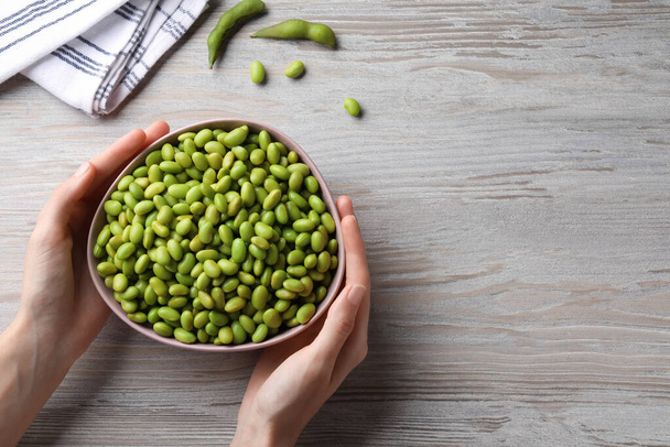 Woman holding bowl of edamame beans at light wooden table, closeup. Space for text - Fotografie, Obrázek