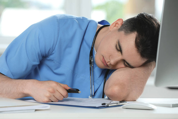 Exhausted doctor sleeping at workplace in hospital - Foto, imagen