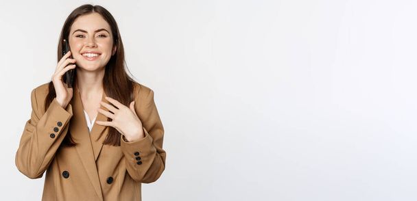 Businesswoman having mobile call, conversation on smartphone, talking with client, standing over white background in brown suit. - Fotografie, Obrázek