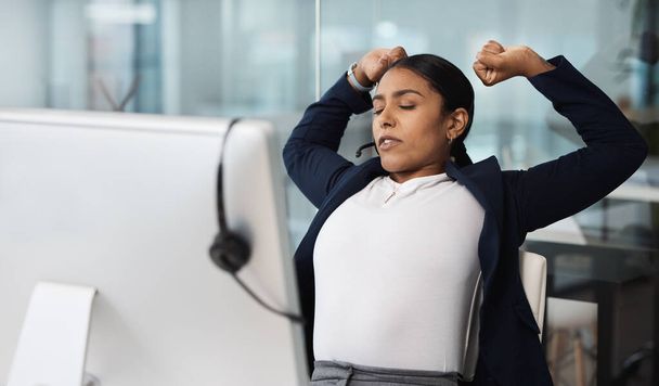 Het was een lange dag van grote verkopen. een jonge zakenvrouw stretching terwijl ze werkt aan haar bureau in een call center - Foto, afbeelding