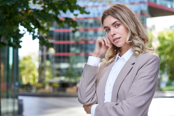 Portrait de femme d'entreprise confiante, jeune femme PDG regarder la caméra, posant en costume beige près des immeubles de bureaux, debout dans la rue. - Photo, image
