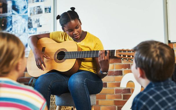 Weve got a future musician among us. a young girl sitting and playing the guitar for her classmates in the classroom at school - Photo, Image