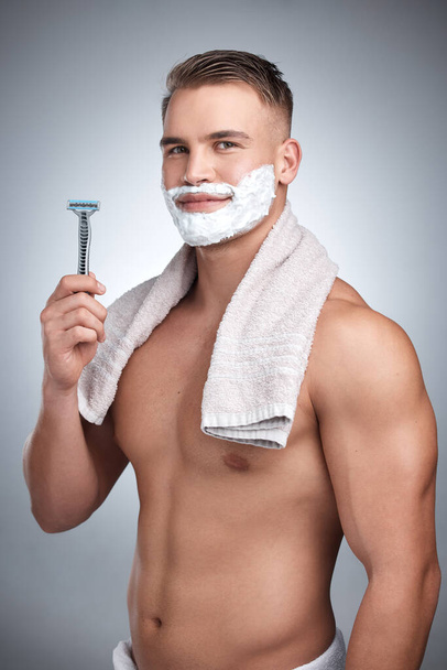 Who would hide this face. Studio portrait of an attractive young man shaving his face against a grey background - Foto, Imagem