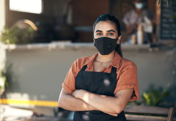 Seguindo regras e regulamentos Covid. uma jovem mulher em pé fora de seu restaurante com os braços dobrados enquanto usava uma máscara facial - Foto, Imagem